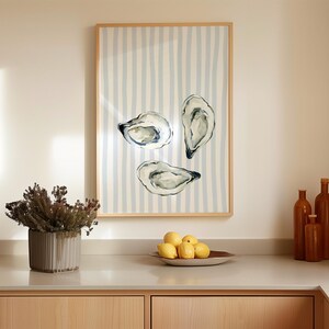 oyster print, coastal kitchen decor, watercolor seafood, preppy wall art, a watercolor painting of three oysters on the half shell, artfully arranged on a background of light blue and white vertical stripes, perfect for a beach house or kitchen.