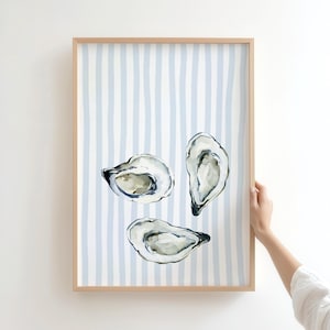 May include: Watercolor print of three oysters in a wooden frame. The background features vertical light blue and white stripes. The oysters are painted in shades of gray and white, with dark accents.