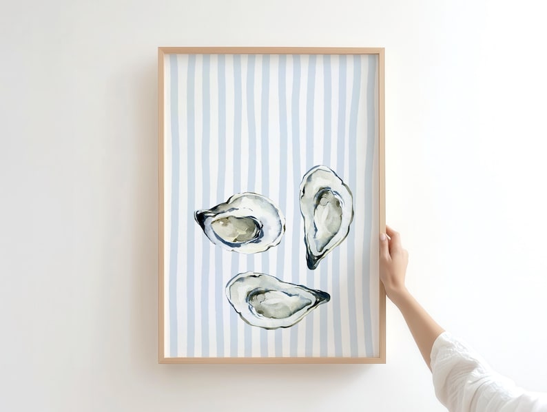 oyster print, coastal kitchen decor, watercolor seafood, preppy wall art, a watercolor painting of three oysters on the half shell, artfully arranged on a background of light blue and white vertical stripes, perfect for a beach house or kitchen.