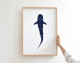 May include: A framed art print featuring a navy blue shark illustration on a white background. The shark is depicted from above, showcasing its dorsal fin and long tail. The artwork is encased in a light brown wooden frame.