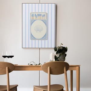 May include: A framed print of a blue and white matchbox with a seashell design on a white background with blue stripes.