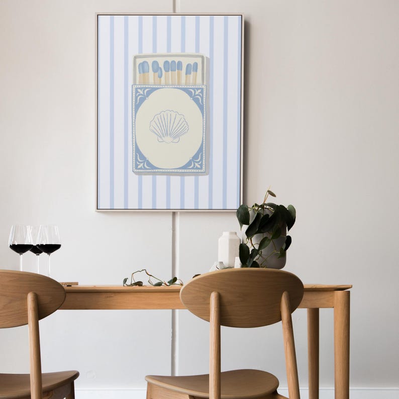 May include: A framed print of a blue and white matchbox with a seashell design on a white background with blue stripes.
