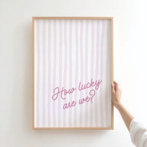 coastal cowgirl decor, pink wall art set, how lucky are we, preppy prints, a gallery wall set of three framed prints in a pink, coastal cowgirl style: one with a bikini on a clothesline, one with the quote 'How lucky are we?' on a striped background, and one with a pair of pink cowboy boots.