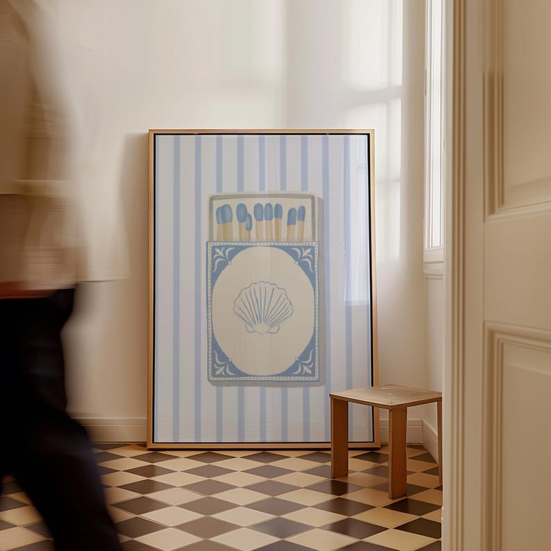 May include: A framed print of a blue and white matchbox with a seashell design on a white background. The matchbox is on a blue and white striped background.
