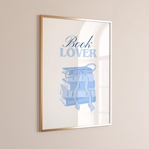 May include: Framed art print featuring a stack of blue books tied with a ribbon. The words "Book Lover" are written above the books in a matching blue font. The frame is gold.