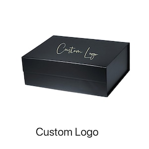 May include: A black rectangular box with a magnetic closure. The box has a gold script font that reads "Custom Logo" on the lid. The box is sitting on a white background.