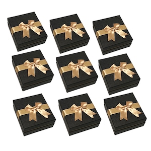 May include: Nine black gift boxes with gold satin ribbon bows. The boxes are square and have a textured surface. The gold ribbon is tied in a bow on top of each box. The boxes are arranged on a white background.