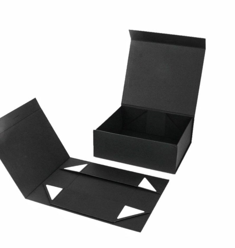 May include: Black folding gift box with a magnetic closure. The box is open, revealing the interior. The lid is open and the box is partially assembled. White triangular accents are visible on the inside flaps.