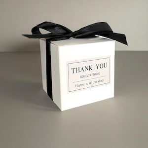 May include: A white gift box with a black satin ribbon bow. The box has a black stripe down the side and a label that reads "THANK YOU FOR EVERYTHING, Have a nice day."