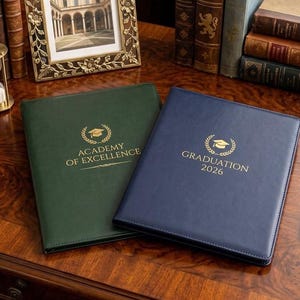 May include: A dark green folder with the gold text ACADEMY OF EXCELLENCE and a graduation cap icon, alongside a navy blue folder with the gold text GRADUATION 2026 and a graduation cap icon, both featuring stitched edges and a smooth finish.