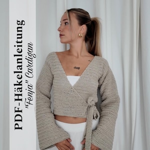 Op de afbeelding: Een beige gehaakt wikkelvest met lange mouwen, een V-hals en klokmouwen. De tekst "PDF-Häkelanleitung "Fenja" Cardigan" staat aan de linkerkant van de afbeelding.