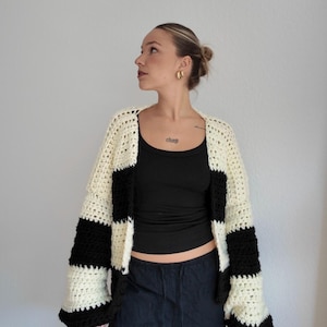 Pode incluir: Um cardigan de croch&ecirc; feito &agrave; m&atilde;o com um padr&atilde;o arrojado de listras pretas e creme. O su&eacute;ter de frente aberta apresenta mangas largas e um ajuste descontra&iacute;do. A pe&ccedil;a &eacute; uma adi&ccedil;&atilde;o elegante a qualquer guarda-roupa.