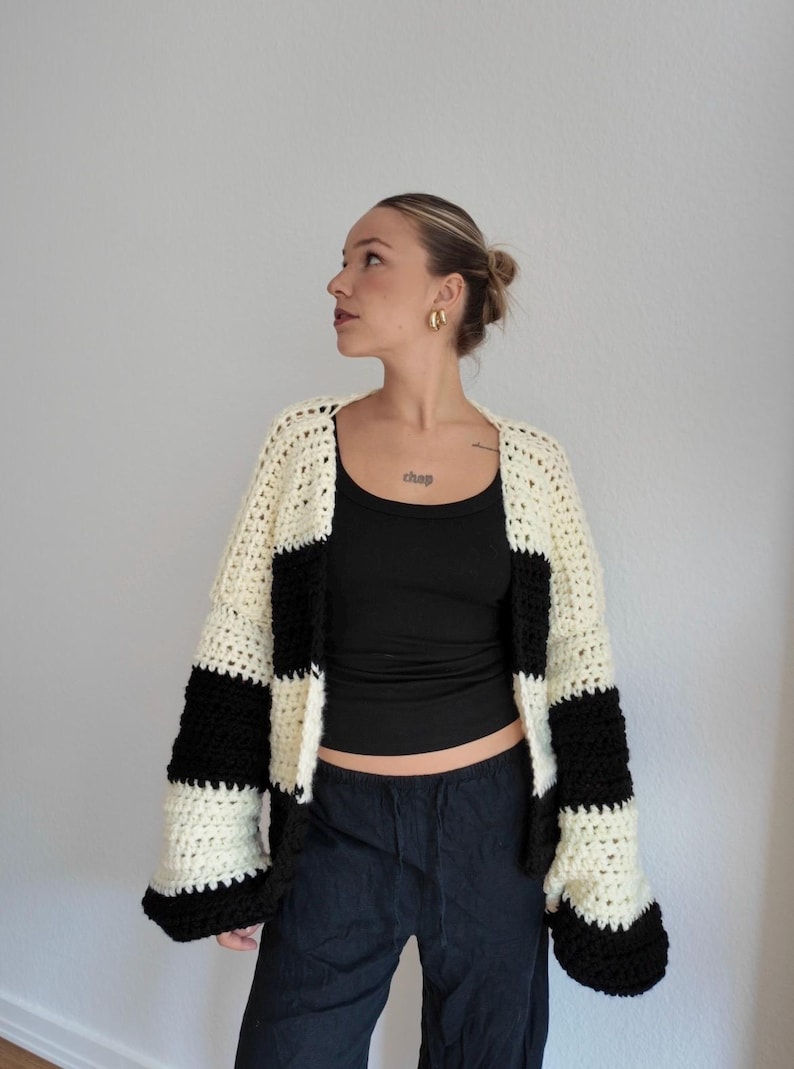 Pode incluir: Um cardigan de croch&ecirc; feito &agrave; m&atilde;o com um padr&atilde;o arrojado de listras pretas e creme. O su&eacute;ter de frente aberta apresenta mangas largas e um ajuste descontra&iacute;do. A pe&ccedil;a &eacute; uma adi&ccedil;&atilde;o elegante a qualquer guarda-roupa.