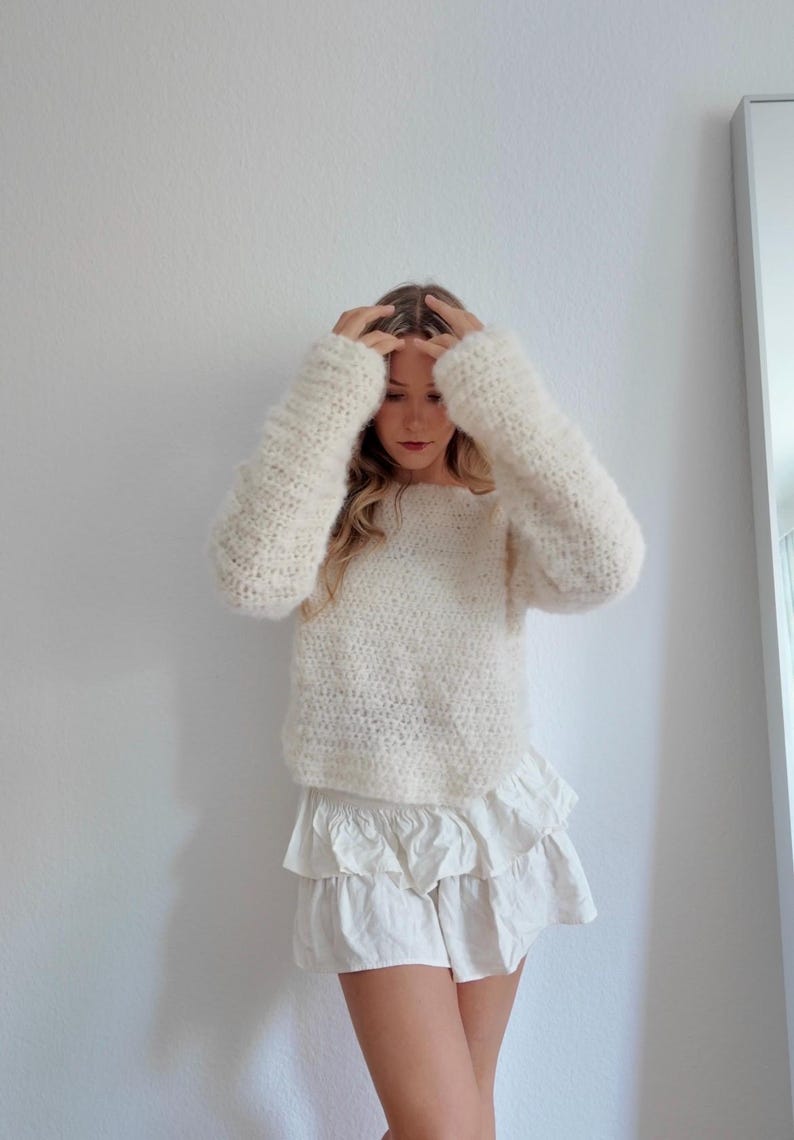 May include: Cream-colored, long-sleeved sweater with a textured knit. The sweater is paired with a white, tiered skirt. The outfit is casual and comfortable, suitable for everyday wear.