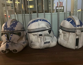 May include: Three white and blue plastic helmets with a weathered look. The helmets have a blue stripe across the top and a black visor.