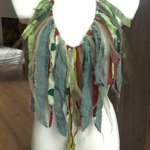 May include: A halter top constructed from multiple vertical strips of fabric in shades of sage green, olive, dark red, and muted blue. The strips feature frayed edges and varying textures, including sheer mesh and solid cotton, creating a layered effect.