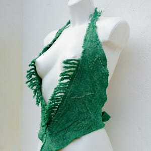 Può includere: Un top all'americana verde realizzato in tessuto strutturato con un bordo sfrangiato. Il top è esposto su un manichino bianco. Il top all'americana ha un design unico con bordi grezzi.
