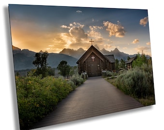 May include: A scenic photograph of a wooden chapel with a cross on top, set against a backdrop of mountains and a sunset sky. A wooden walkway leads to the chapel, surrounded by greenery.