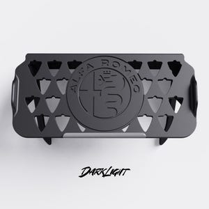 May include: A matte black car accessory featuring the Alfa Romeo logo in the center. The accessory has a rectangular shape with triangular cutouts and the text "DARKLIGHT" in a script font.