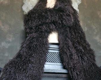 May include: A mannequin head wearing a black top hat, a white ruffled collar, and a long, dark brown, shaggy scarf. The scarf is draped over the mannequin's shoulders, creating a dramatic effect. The background is a muted, textured wall.