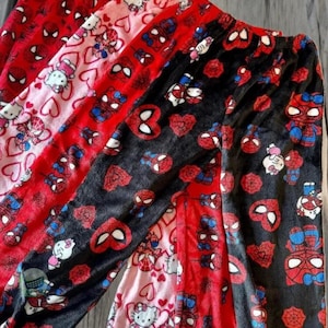 Puede incluir: Tres pares de pantalones de pijama con diferentes patrones. El primer par es rosa con corazones blancos y un personaje de Hello Kitty. El segundo par es rojo con un personaje de Spiderman y corazones blancos. El tercer par es negro con un personaje de Spiderman y corazones rojos.