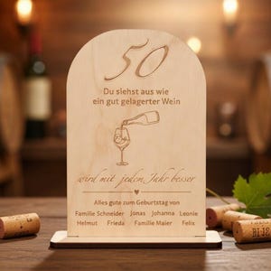 Könnte beinhalten: Handgefertigtes Holzschild mit dem Wort "Welcome" in verspielter Schrift. Es hat einen weißen, abgenutzten Hintergrund und einen dunkelbraunen Rahmen, ideal für eine Eingangstür. Das Schild ist etwa 30 cm breit und 15 cm hoch.