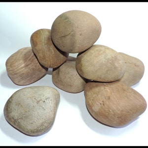 May include: A group of seven smooth, brown river rocks of various sizes. The rocks are arranged in a pile, with the largest rock at the top.