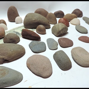 Pu&ograve; includere: Una collezione di ciottoli di fiume lisci e arrotondati in varie tonalit&agrave; di marrone, grigio e rosso. I ciottoli sono disposti su una superficie bianca.