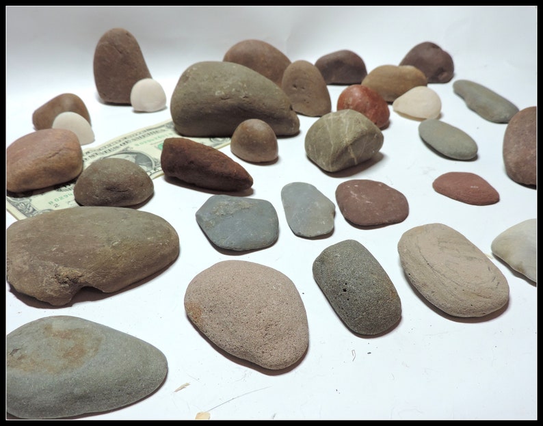 Pu&ograve; includere: Una collezione di ciottoli di fiume lisci e arrotondati in varie tonalit&agrave; di marrone, grigio e rosso. I ciottoli sono disposti su una superficie bianca.