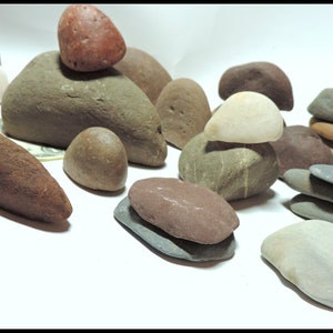 Pu&ograve; includere: Una collezione di pietre lisce di varie forme e dimensioni, di colore grigio, marrone e rosso. Alcune pietre sono impilate l'una sull'altra.
