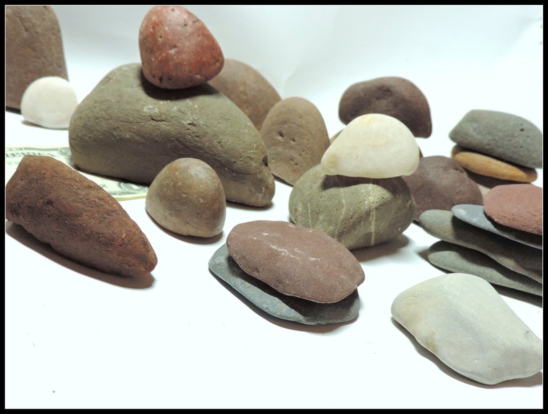 Pu&ograve; includere: Una collezione di pietre lisce di varie forme e dimensioni, di colore grigio, marrone e rosso. Alcune pietre sono impilate l'una sull'altra.