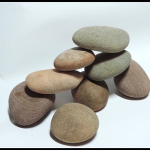 May include: A collection of smooth, rounded stones in various earth tones, including shades of brown, tan, and gray. The stones are stacked in a balanced arrangement, creating a natural, organic display. The stones vary in size and shape.
