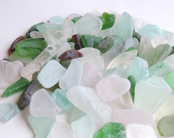 May include: A pile of sea glass in various shades of green, white, and brown. The glass is smooth and polished from being tumbled by the ocean.