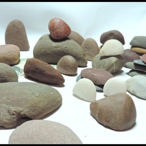 Pu&ograve; includere: Una collezione di pietre lisce e arrotondate in varie tonalit&agrave; di marrone, grigio e bianco. Alcune pietre sono impilate l'una sull'altra, creando piccole torri.