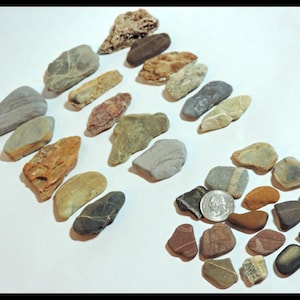 May include: A collection of smooth, colorful stones of various shapes and sizes. Some stones are gray, brown, red, and white. A silver coin is included in the collection.