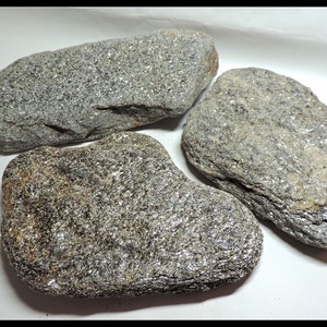 May include: Three smooth, gray stones with a sparkly, glittery texture. The stones are various sizes and shapes.