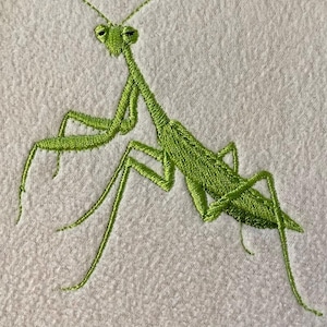May include: A detailed embroidery of a green praying mantis on a white fabric. The insect is depicted with intricate stitching, showcasing its slender body, long legs, and prominent eyes. The artwork captures the mantis's distinctive posture.