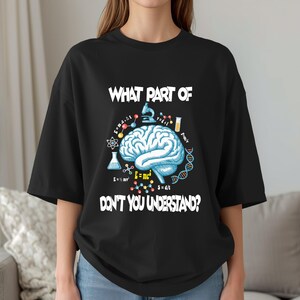 Puede incluir: Camiseta negra con un gráfico de temática científica. El diseño presenta un cerebro azul, fórmulas científicas y el texto "WHAT PART OF DON'T YOU UNDERSTAND?" en blanco. La camiseta tiene mangas cortas y un corte holgado.
