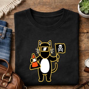 May include: Black t-shirt featuring a cartoon cat wearing a welding mask and holding a traffic cone and a flag with a skull and crossbones. The cat has a white belly and yellow outline.