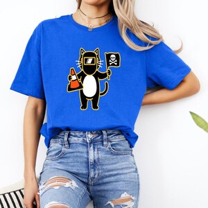 May include: Royal blue t-shirt featuring a cartoon cat wearing a welding mask and holding a traffic cone and a pirate flag with a skull and crossbones. The cat is black with a white belly and yellow outline.