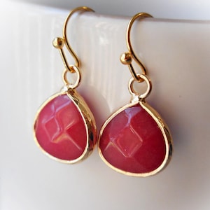 Op de afbeelding: Een paar gouden oorhangers met roze gefacetteerde edelsteen druppels.