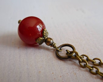 May include: A red carnelian gemstone pendant on a bronze chain. The pendant has a decorative bronze leaf design.