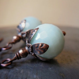 May include: A pair of earrings with light blue gemstone beads and copper-toned metal accents. The beads are faceted and have a delicate, feminine look.