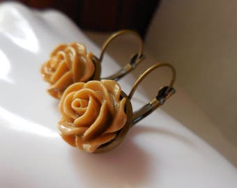 May include: A pair of bronze hoop earrings with a beige rose charm on each earring.