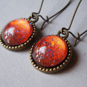 May include: A pair of bronze earrings with red and blue glitter embedded in the round glass cabochons.