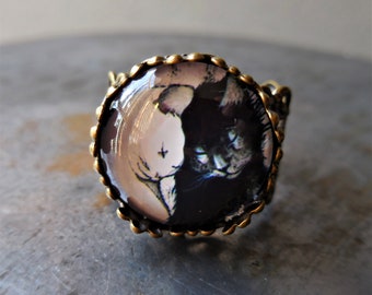 May include: A black and white cat ring with a bronze setting. The cat is depicted in a yin yang style with a white cat on one side and a black cat on the other.