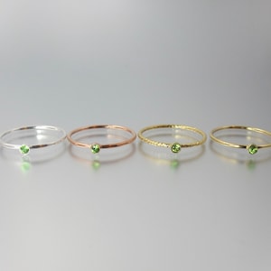 May include: Four delicate rings each featuring a single green gemstone. The rings are in silver, rose gold, gold, and a braided gold style.