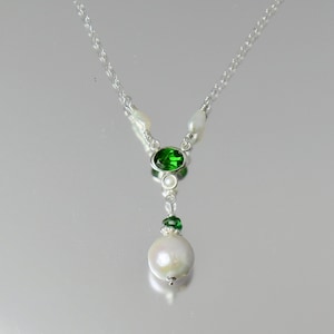 Peut inclure: Un collier en argent avec un pendentif en pierre précieuse verte et une perle blanche. Le collier est accentué de petites perles blanches.