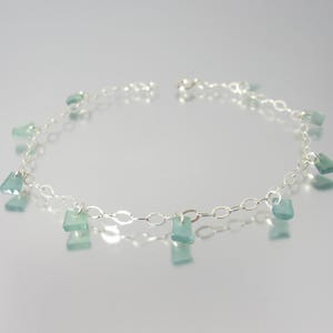 May include: A silver chain bracelet featuring multiple small, translucent, pale green rectangular charms spaced evenly along the links. The bracelet is constructed with a delicate metal chain and secure jump rings holding each individual stone-like piece.