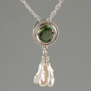May include: A silver necklace featuring a round, faceted green gemstone set in a twisted metal frame, with a cluster of three elongated, irregular white pearls suspended from the bottom of the setting on a silver chain.